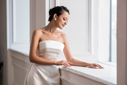 Woman in a strapless white dress sitting by a window