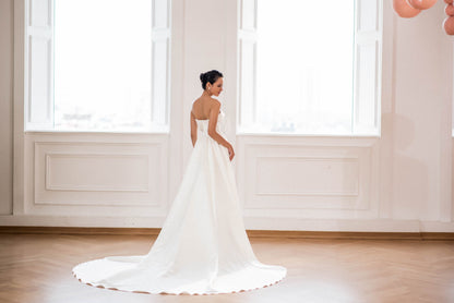 Woman in a white wedding dress standing in a room with large windows.