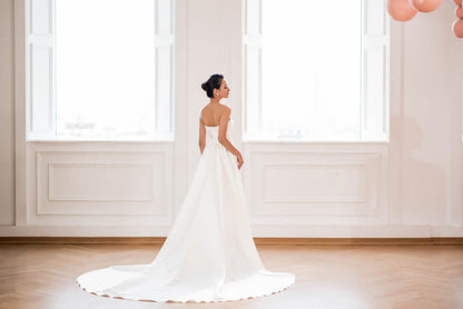Woman in a white wedding dress standing in a room with large windows.