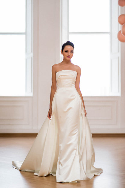 Woman wearing a strapless white wedding dress in a bright room with large windows.