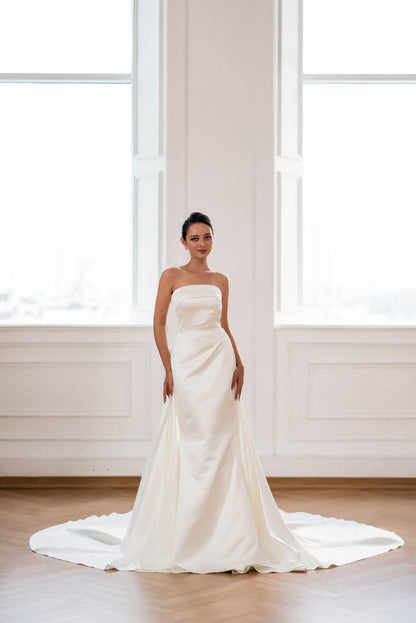 Woman wearing a strapless white wedding dress in a room with large windows.