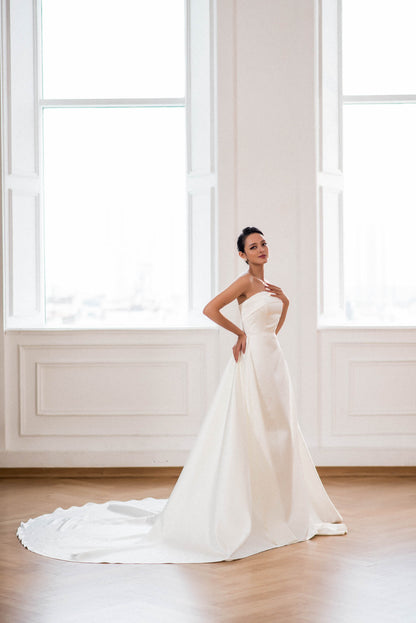 Woman in a white wedding dress standing in a room with large windows.