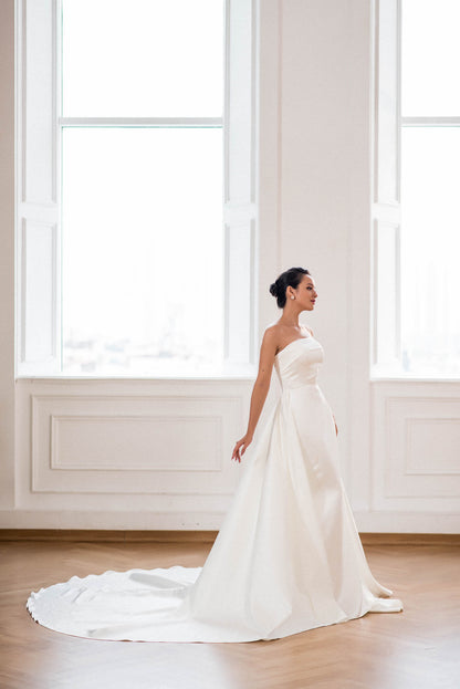 Woman in a white wedding dress standing in a room with large windows.