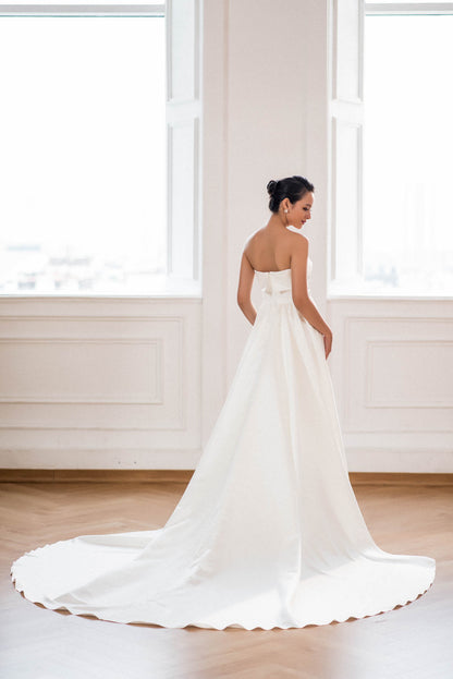 Woman in a white wedding dress standing in a room with large windows.