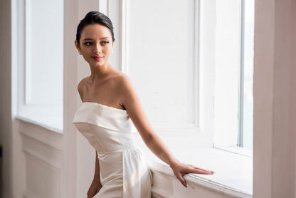 Woman in a white dress sitting by a window in a bright room