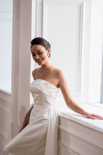 Woman in a white strapless dress sitting by a window with soft lighting