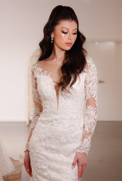 Woman wearing a white lace wedding dress with long sleeves indoors.