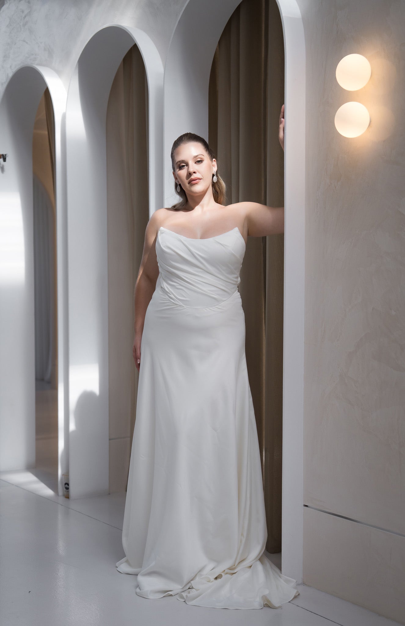 Woman in a white strapless gown standing in a modern architectural setting with arched doorways.