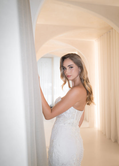 Woman in a white wedding dress standing in a softly lit room with geometric wall design.