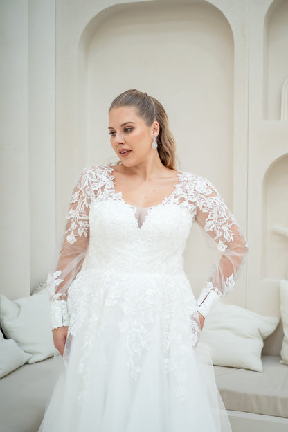 Woman wearing a white wedding dress with lace sleeves in a softly lit room.