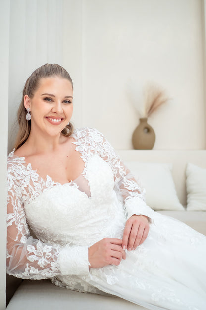 Woman in a white lace wedding dress sitting on a couch.