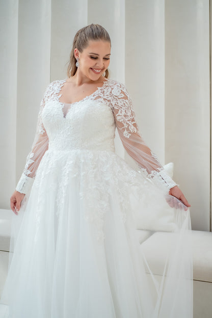 Woman wearing a white wedding dress with lace sleeves against a neutral background