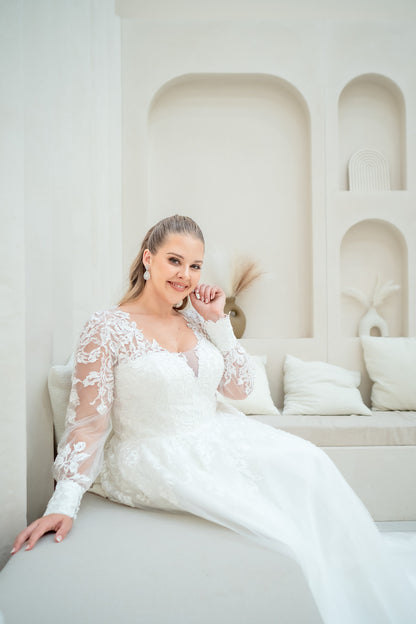 Woman in a white wedding dress sitting on a white couch in a minimalist room.