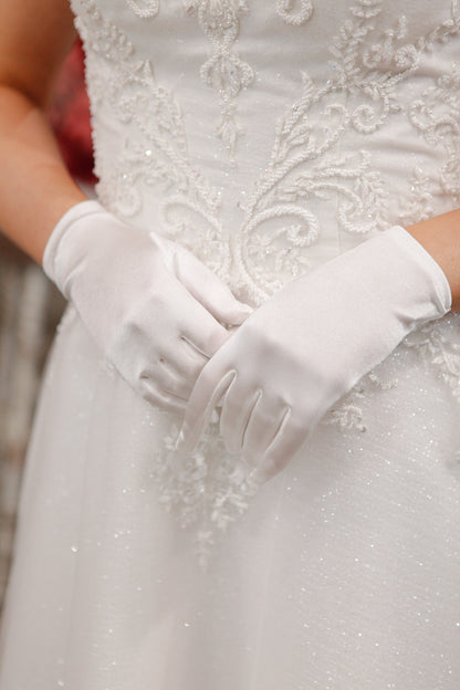 White gloves being worn with a detailed white dress.