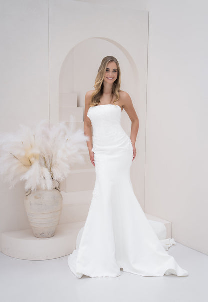 Woman in a white strapless gown standing in a minimalistic room with decorative elements.