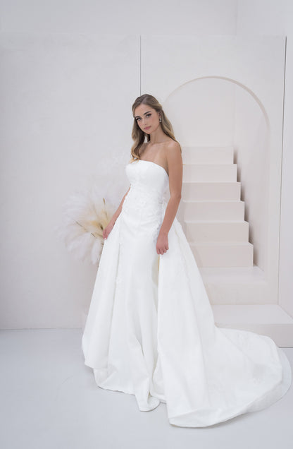 Woman in a white strapless gown standing in front of a white wall with steps.