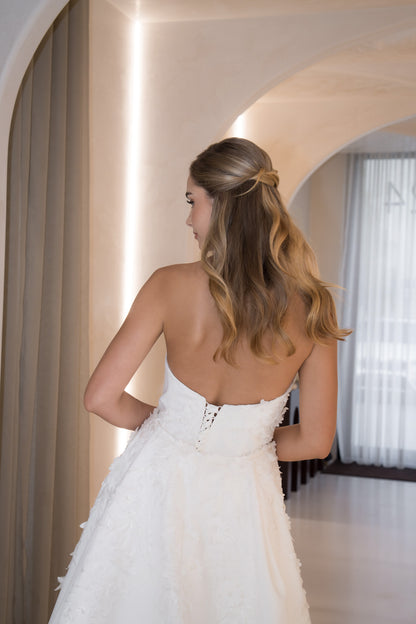 Woman in a white wedding dress standing in a softly lit room with neutral decor.