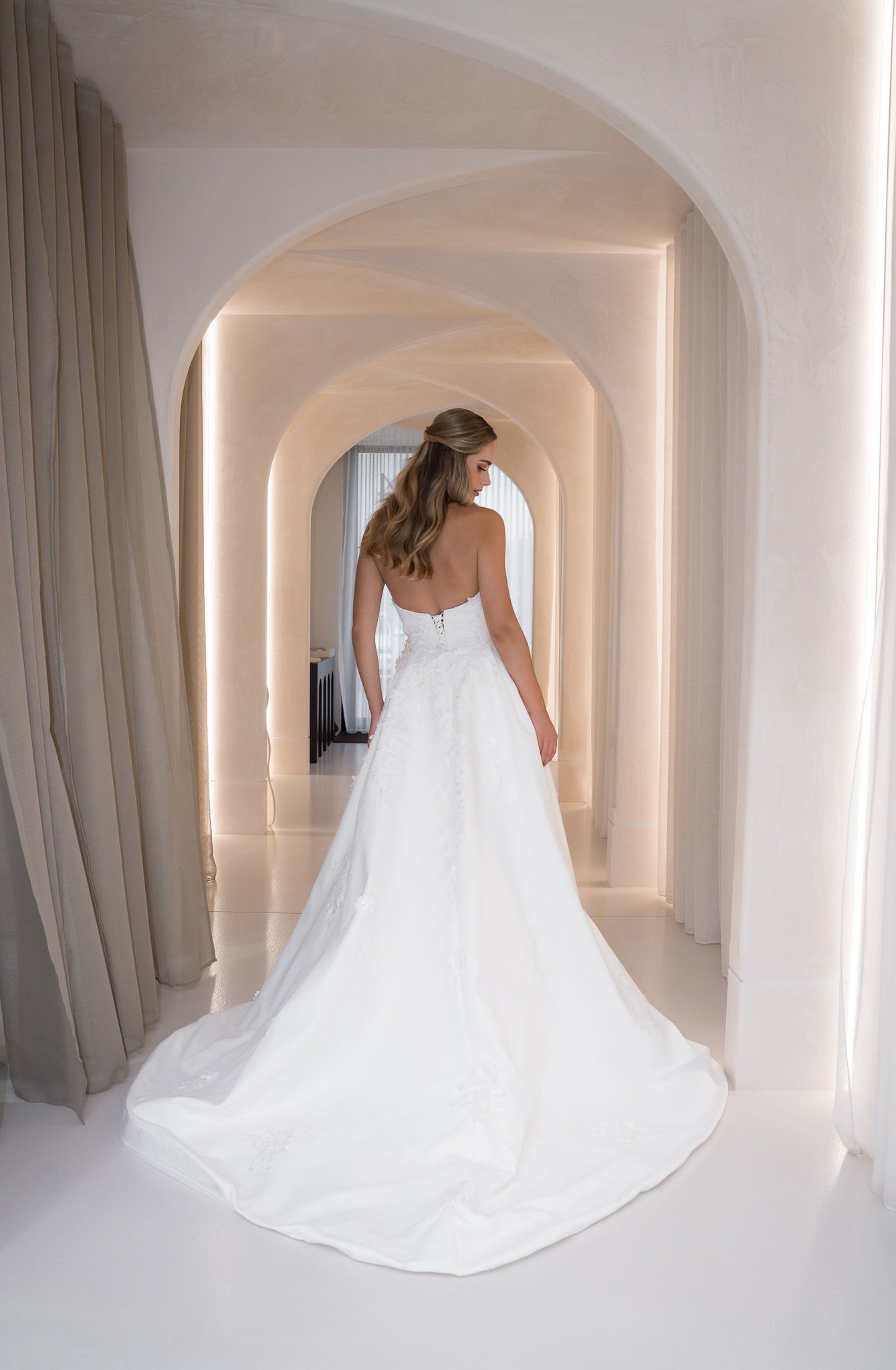 Woman in a white wedding dress standing in a hallway with arches.