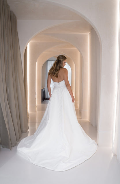 Woman in a white wedding dress standing in a hallway with arches.