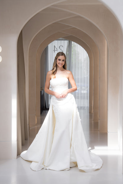 Woman in a white wedding dress standing in an elegant hallway with arches.