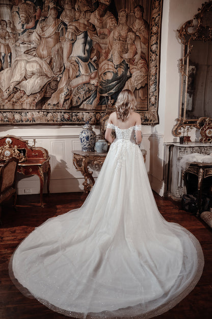 Woman in a white wedding dress standing in a room with classical decor.