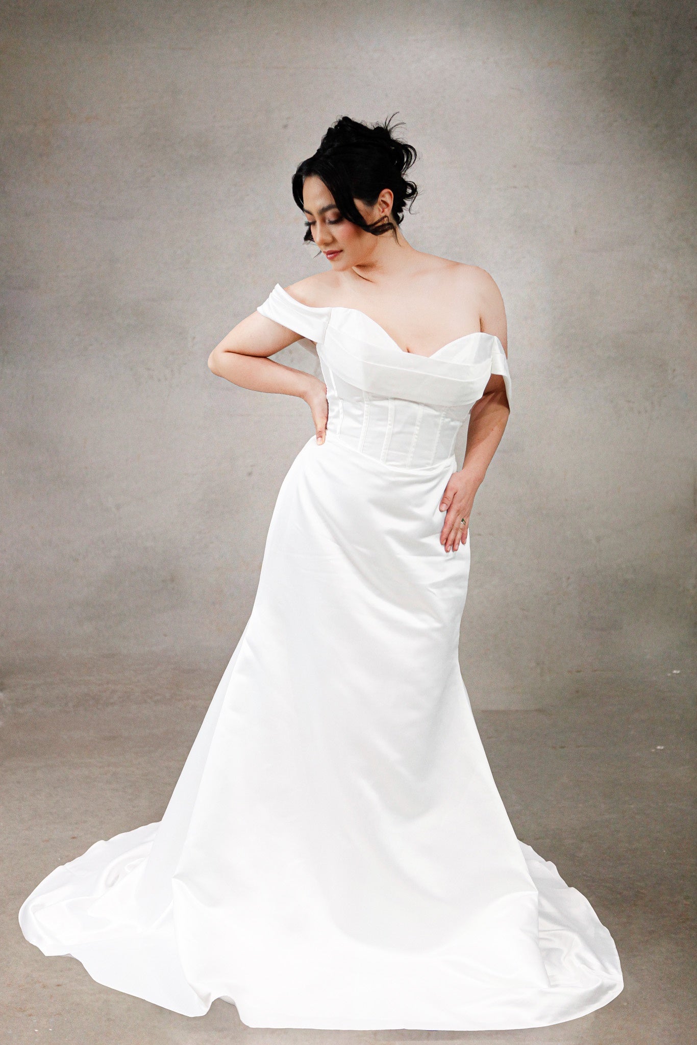 Woman wearing a white off-shoulder wedding dress against a plain background