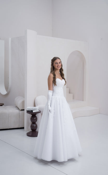 Woman in a white wedding dress standing in a minimalist room with white walls and furniture.