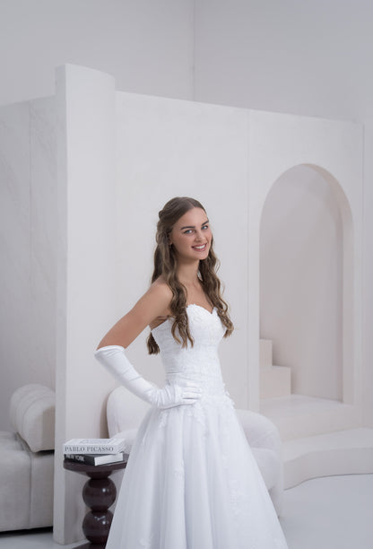 Woman in a white wedding dress with long gloves standing in a minimalistic room.