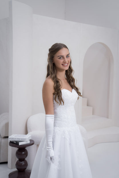 Woman in a white dress with long gloves standing in a minimalist room.