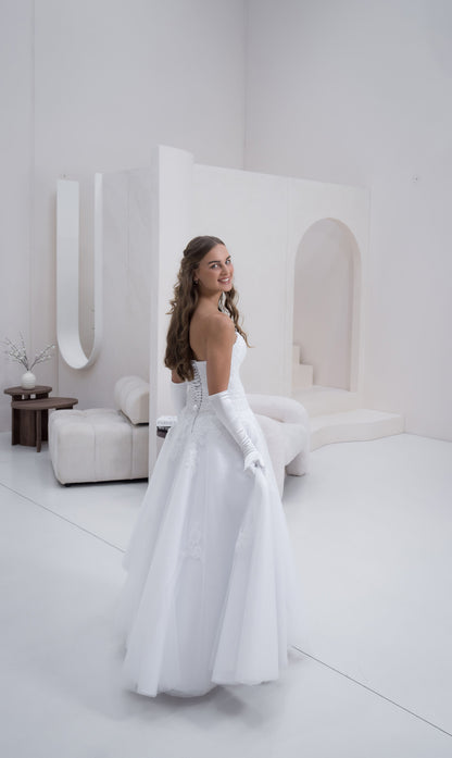 Woman in a white wedding dress standing in a minimalist room with white furniture.