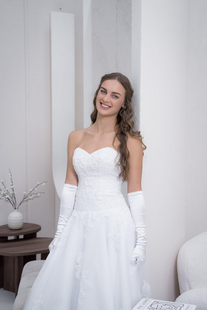 Woman in a white wedding dress with gloves standing against a neutral background