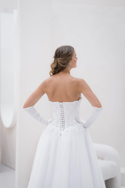 Woman in a white strapless gown with long gloves standing against a white background