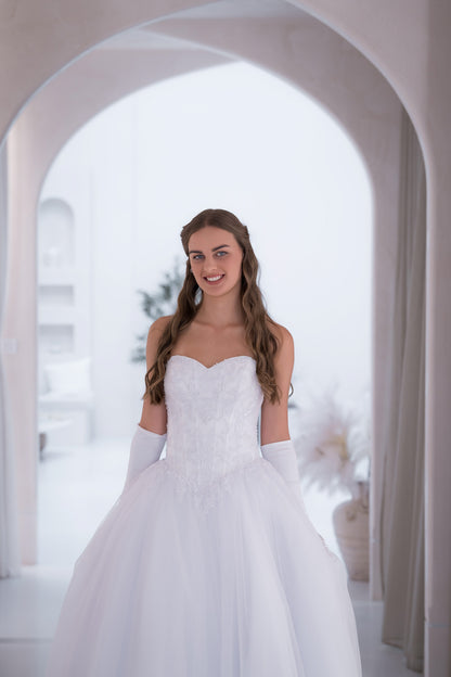 Woman in a white wedding dress standing in a bright, arched doorway.