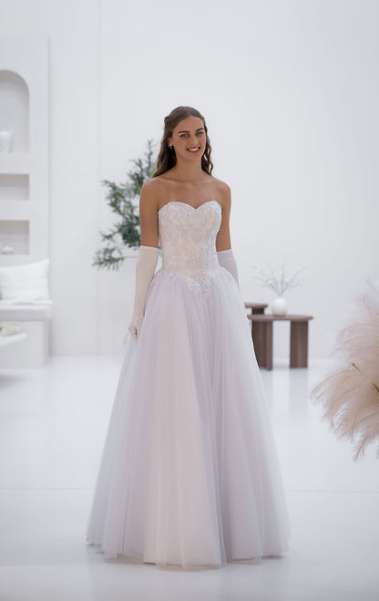 Woman in a white wedding dress standing in a bright room with minimal decor.