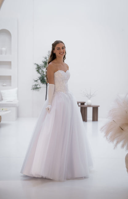 Woman in a white wedding dress standing in a bright, minimalistic room.
