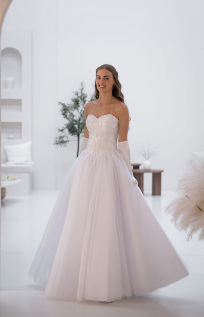 Woman wearing a white strapless wedding dress in a bright room.