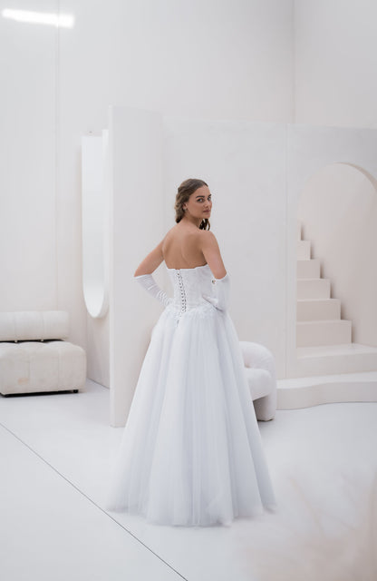 Woman in a white strapless gown standing in a minimalist room with white furniture.