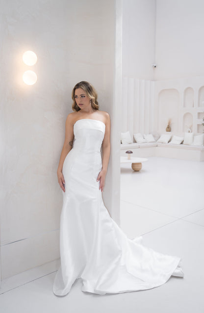 Woman in a strapless white wedding dress standing in a minimalistic room.