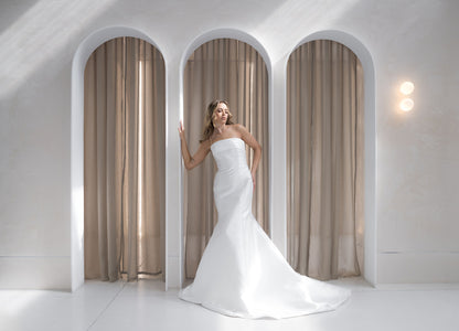 Woman in a white wedding dress standing in a modern interior with arched doorways and beige curtains.
