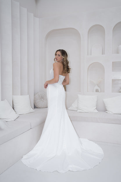 Woman in a white strapless gown standing in a minimalist white room.