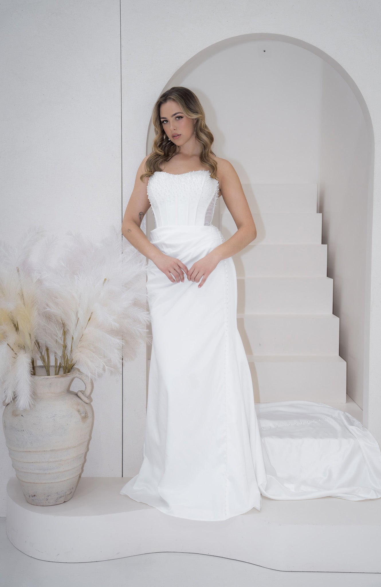 Woman in a white strapless gown standing in a minimalistic setting with a white arch and vase.