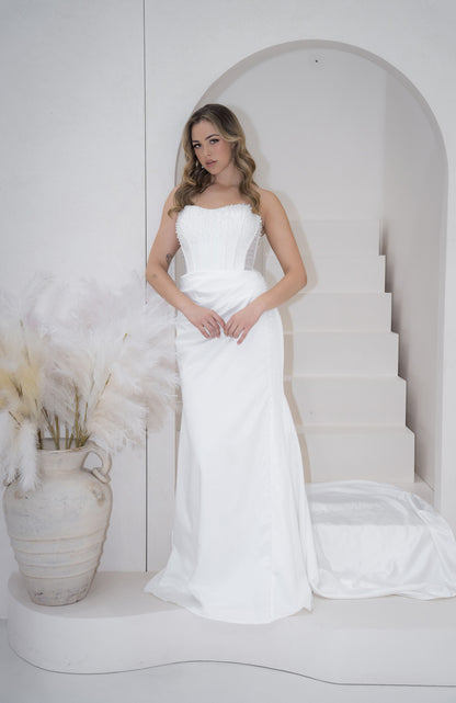 Woman in a white strapless gown standing in a minimalistic setting with a white arch and vase.