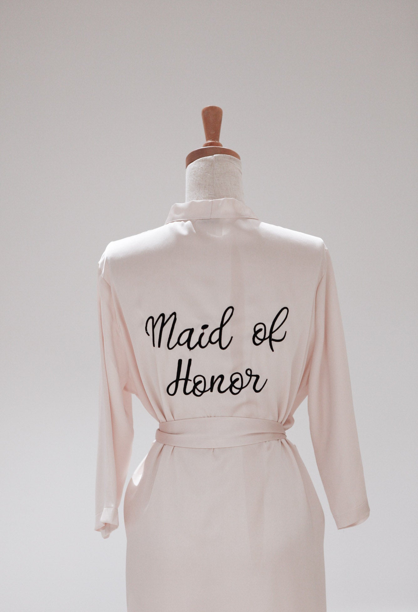 Pink robe with 'Maid of Honor' text on a mannequin against a white background