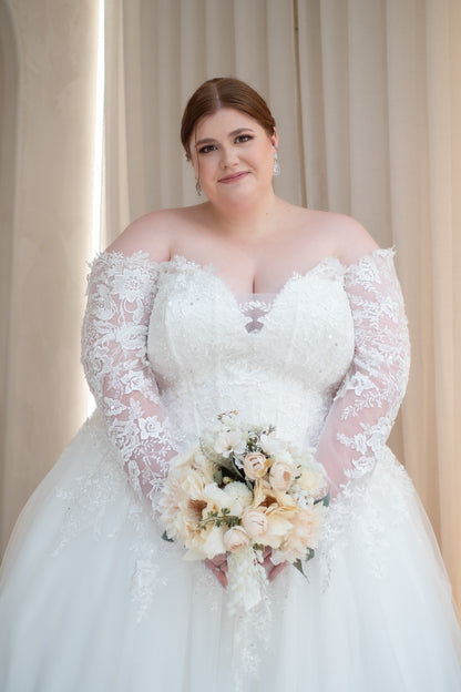 Woman in a white wedding dress holding a bouquet against a beige curtain background