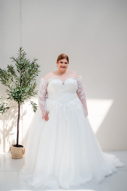 Woman in a white wedding dress standing next to a potted plant against a plain background