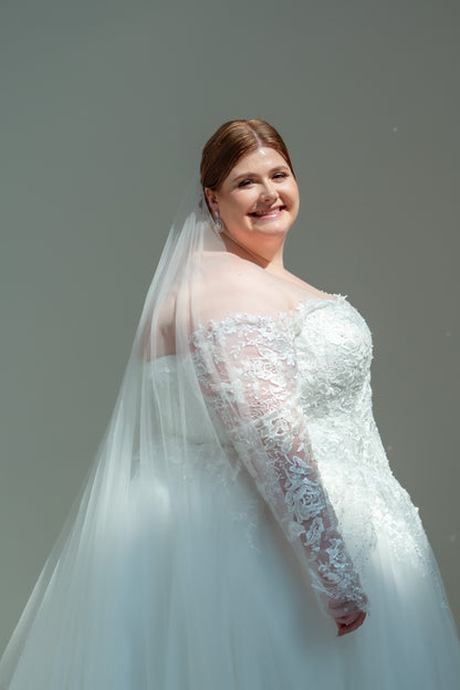 Woman in a white wedding dress with a long veil against a plain background