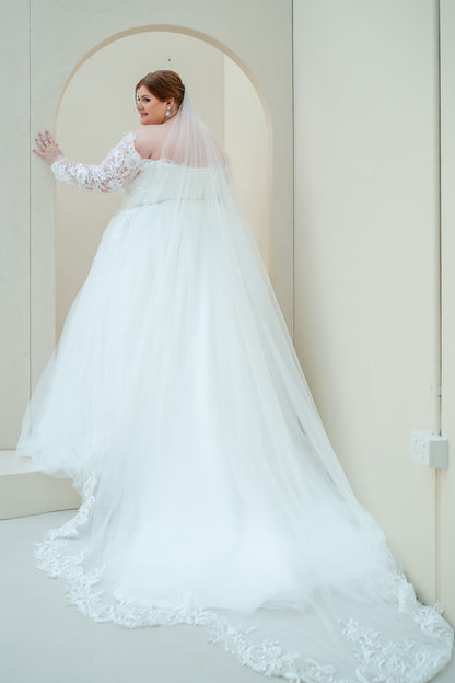 Woman in a white wedding dress with a long train standing in a room with a neutral color scheme.