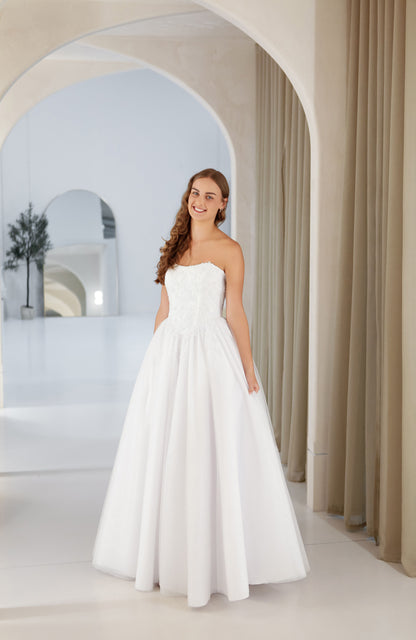 Woman in a strapless white wedding dress standing in a bright, arched room.