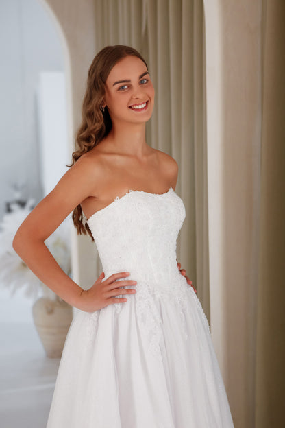 Woman wearing a strapless white wedding dress indoors.