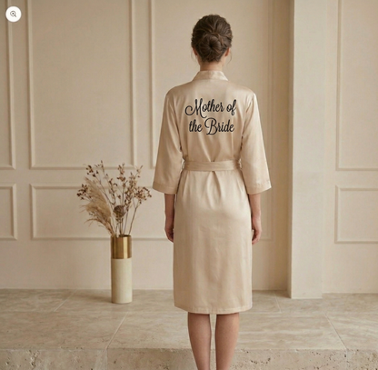 Woman wearing a beige 'Mother of the Bride' robe in a room with a vase of dried flowers.